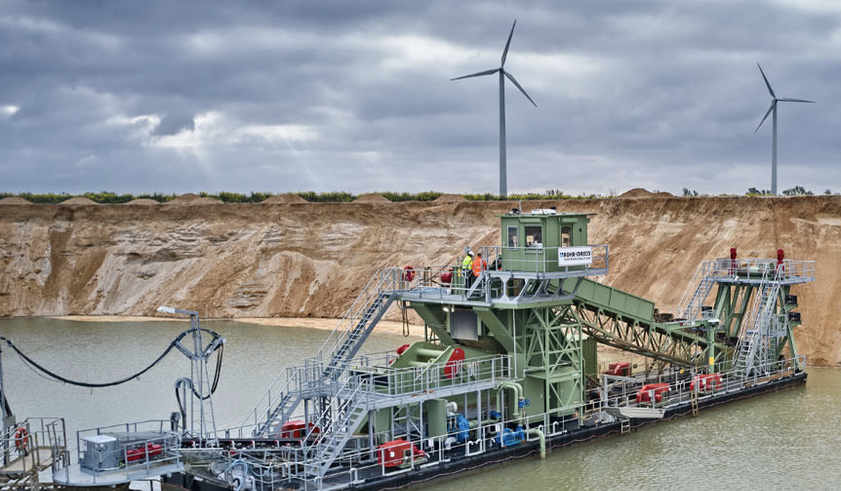 photo of green dredge mine with wind turbines